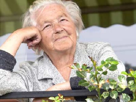 Alte Frau steht am Balkon und lächelt